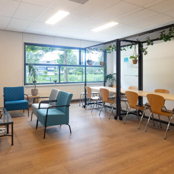 zithoek met salontafel en fauteuils en vergadertafels met stoelen