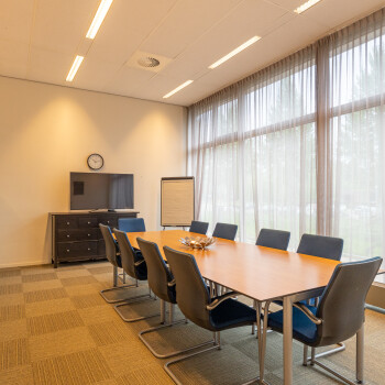 vergaderuimte met tafels en blauwe stoelen, raampartij met witte vitrage