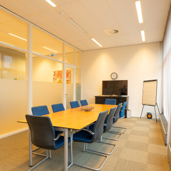vergaderruimte met tafels en daaromheen blauwe stoelen. Tv en flipover.