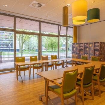 vergaderruimte met tafels in  U-opstelling met daaromheen groene stoelen, aan de achterzijde een grote raampartij