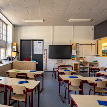 binnenzijde van een klaslokaal met schoolmeubilair voor kleuters. Tafels en stoelen, blauwe vloer.