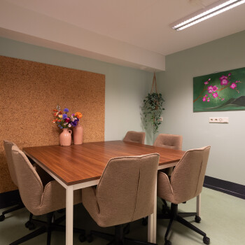 groene achterwand met bruine latjes. vierkante tafel met 6 stoelen, hangplant, schilderij