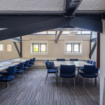 tapijt, vierkante tafel met blauwe stoelen, balken aan plafond