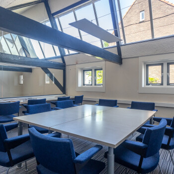 vierkante witte tafel met blauwe stoelen eromheen, hoog raam