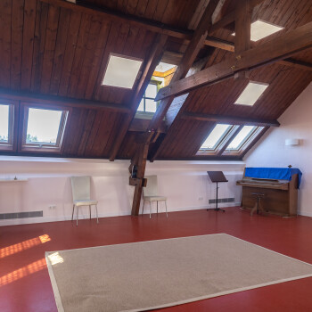 vrije ruimte met vloerkleed en piano en enkele stoelen tegen wand