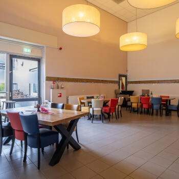 zaal met diverse tafels en stoelen, lampenkappen aan plafond