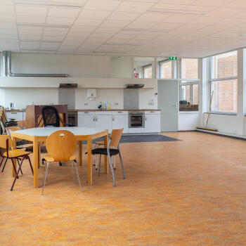 zaal met tafel, stoelen en keukenblok op de achtergrond
