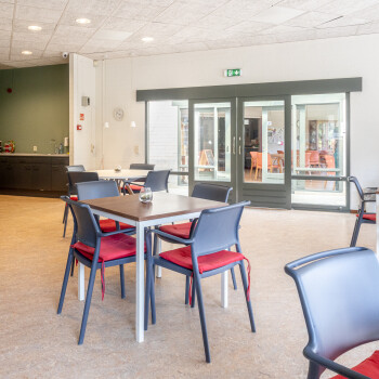 tafel met 4 stoelen, houtkleurige vloer, achterin een gedeelde van een keukenblok